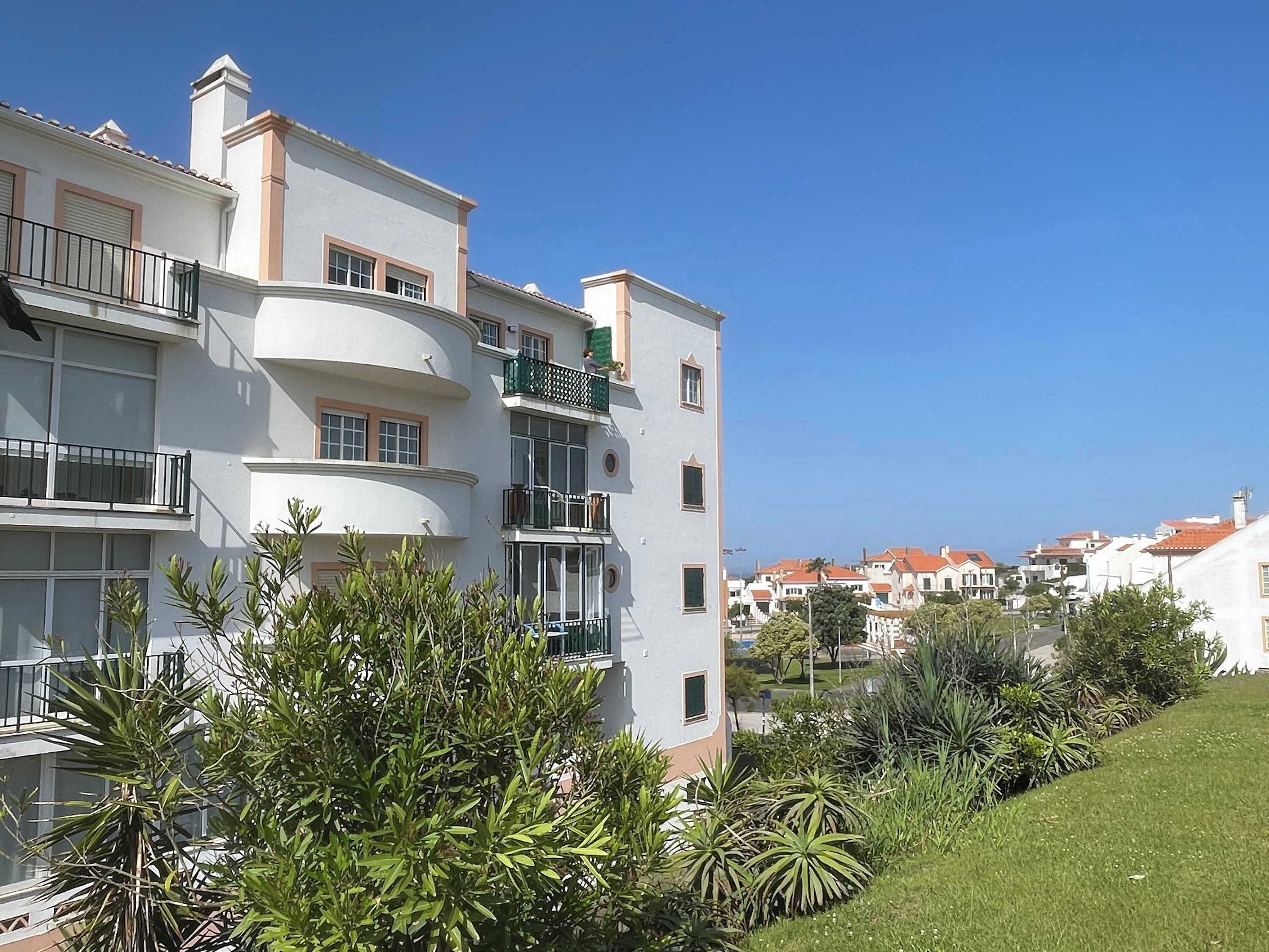 A multi-story residential building with balconies, a well-maintained lawn, and a clear view of the surrounding neighborhood.