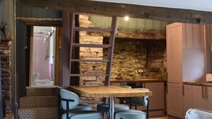 A rustic kitchen with a stone wall, wooden beams, and a wooden table with chairs. - Ty Llaeth 2-bed Cottage, Sleeps 4, Pet Friendly (Carmarthen)