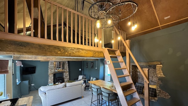 A loft-style living area with a stone fireplace, a sofa, a dining table with chairs, a staircase, and a ceiling light fixture. - Ty Llaeth 2-bed Cottage, Sleeps 4, Pet Friendly (Carmarthen)