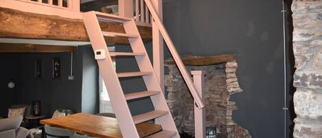 A staircase with a wooden finish, a dining area with a wooden table and chairs, and a stone wall.