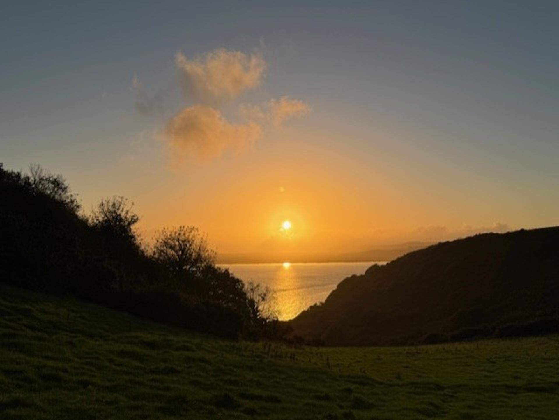 Um pôr do sol sobre a água, com colinas ao primeiro plano.
