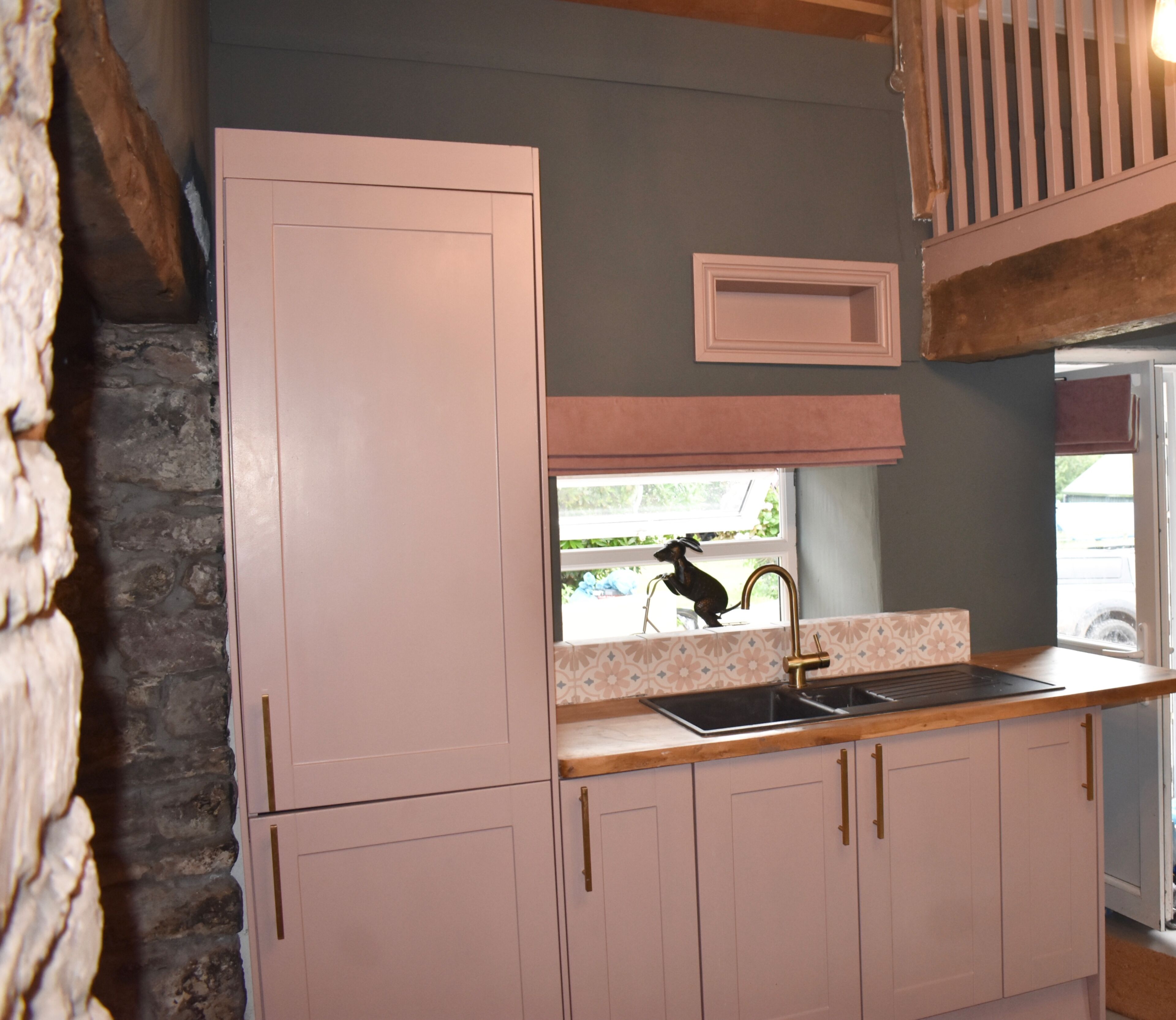A kitchen with pink cabinets, a stone wall, and a window with a view of greenery.