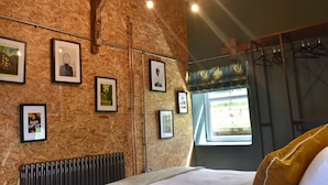 A rustic room with wooden walls, a bed, a radiator, and framed pictures on the wall. - Ty Llaeth 2-bed Cottage, Sleeps 4, Pet Friendly (Carmarthen)