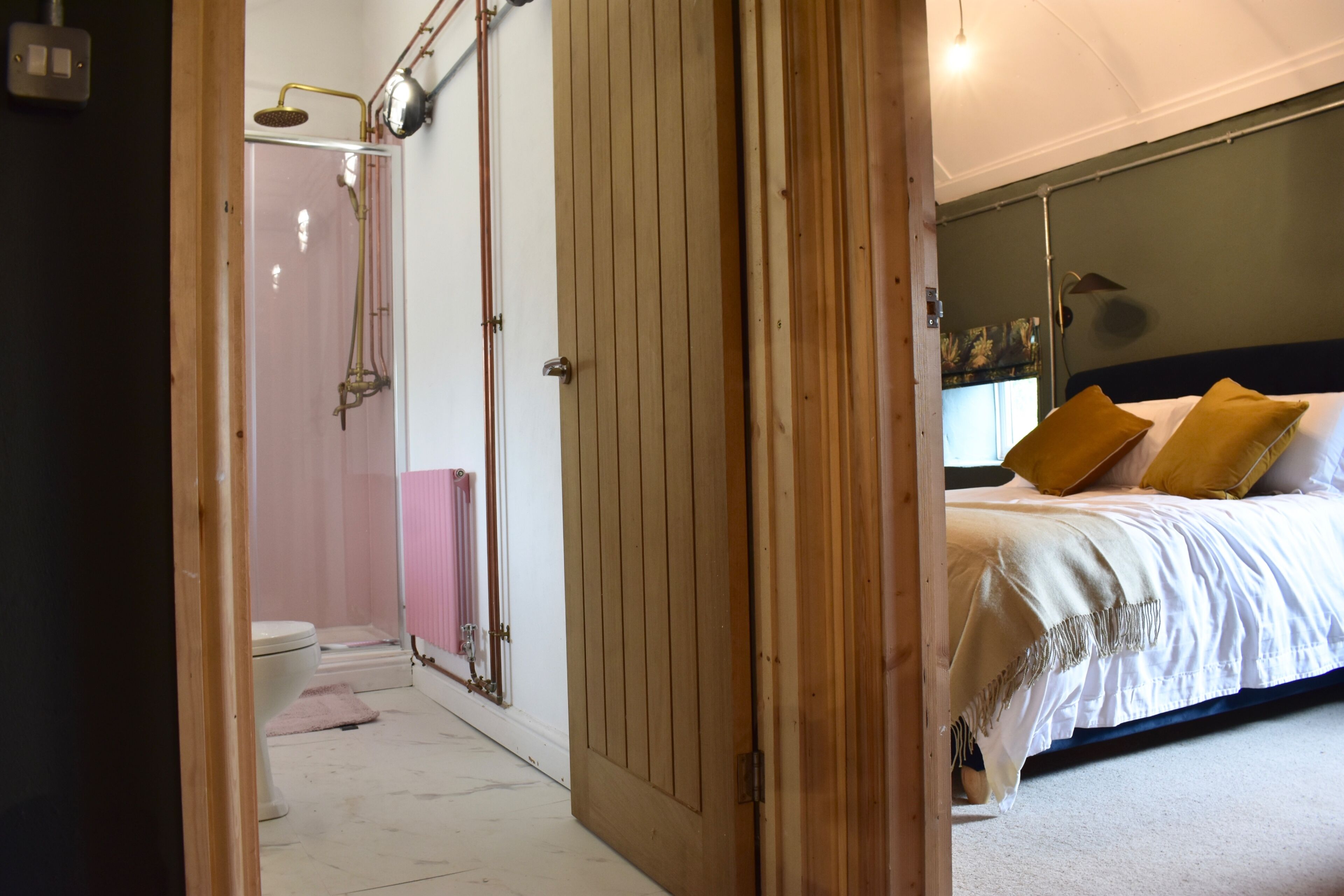 A bedroom with a bed, a wooden door, a mirror, and a shower area.