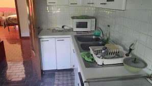Una cucina compatta con mobili bianchi, un forno a microonde, un lavello e un piccolo piano di lavoro.
