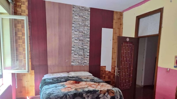 Una stanza con un letto, una porta in legno, un muro di pietra e una finestra.