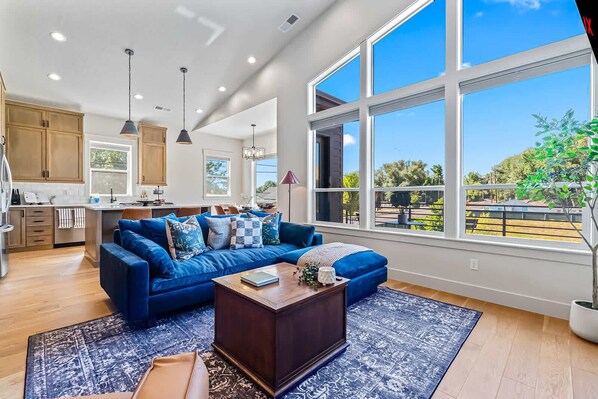 Amplia sala de estar con sofá azul, una mesa de centro y ventanas grandes que ofrecen vistas al exterior.