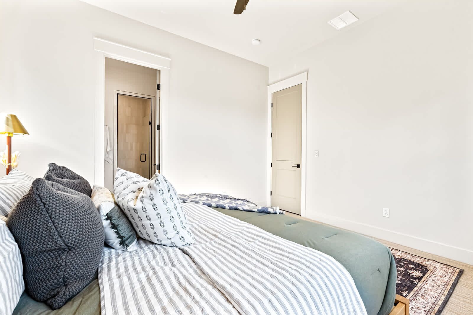 A bedroom with two beds, a bedside table, a lamp, and a door leading to another room.