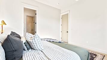 A bedroom with two beds, a bedside table, a lamp, and a door leading to another room.