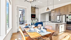 A modern kitchen with stainless steel appliances, a dining area with wooden furniture, and a stone accent wall. - Dark & Sleek 3BR Escape by the Golf Course (Boise)