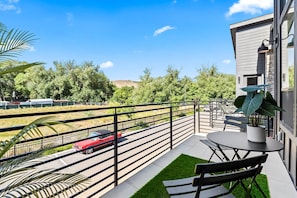 En balkon med et bord, stole, en potteplante og udsigt til en vej med en rød bil.