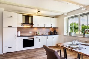 A modern kitchen with white cabinets, a built-in oven, and a dining area with a wooden table and chairs. - Apartment 'Mayerhofer 1' with Private Terrace, Shared Garden and Wi-Fi (Arnstorf)