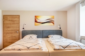 A double bed with a grey headboard, a wooden door, and a wall-mounted abstract painting. - Apartment 'Mayerhofer 1' with Private Terrace, Shared Garden and Wi-Fi (Arnstorf)