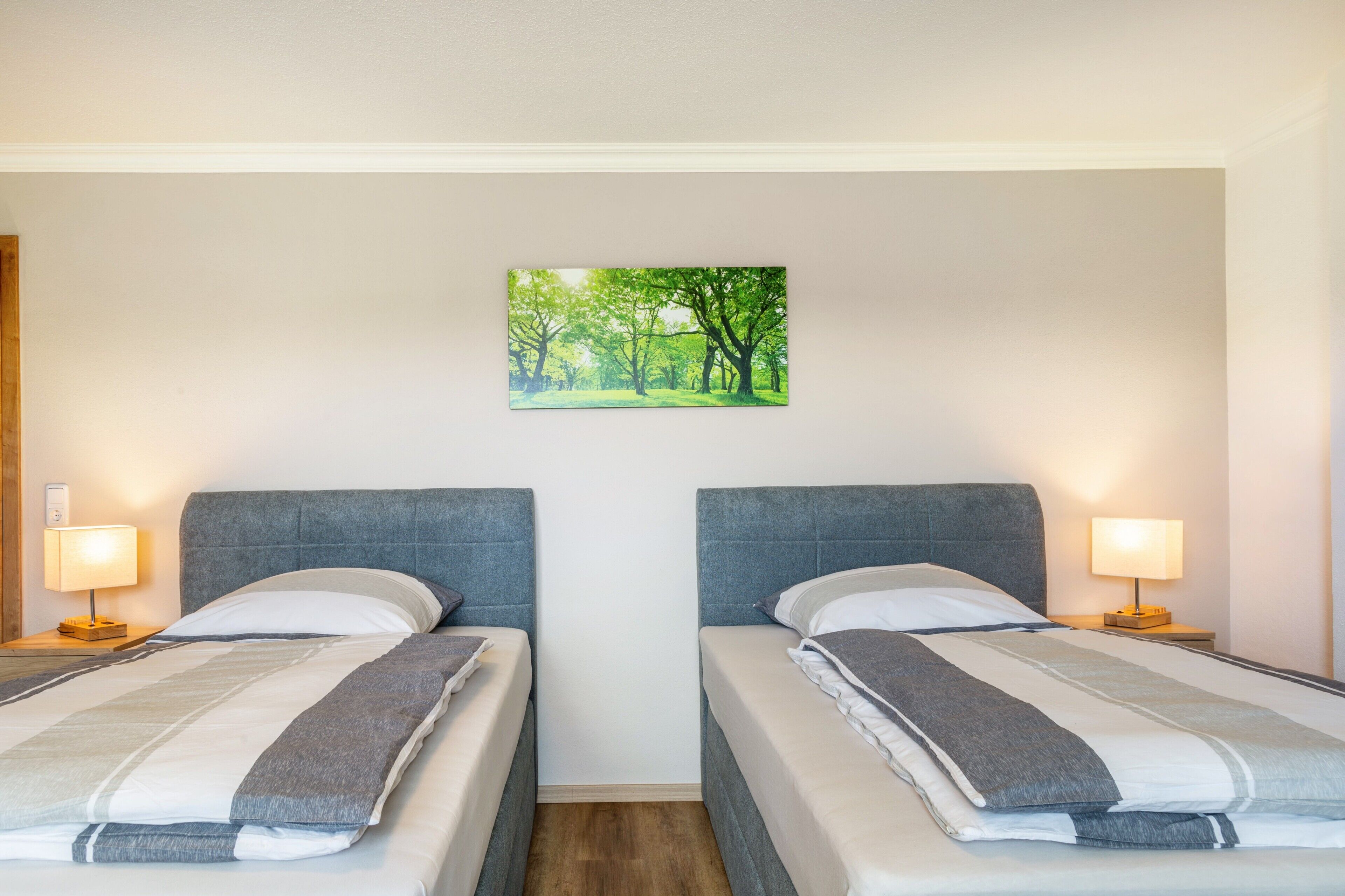 Une chambre d’hôtel avec deux lits, un tableau représentant une forêt et des lampes de chevet.