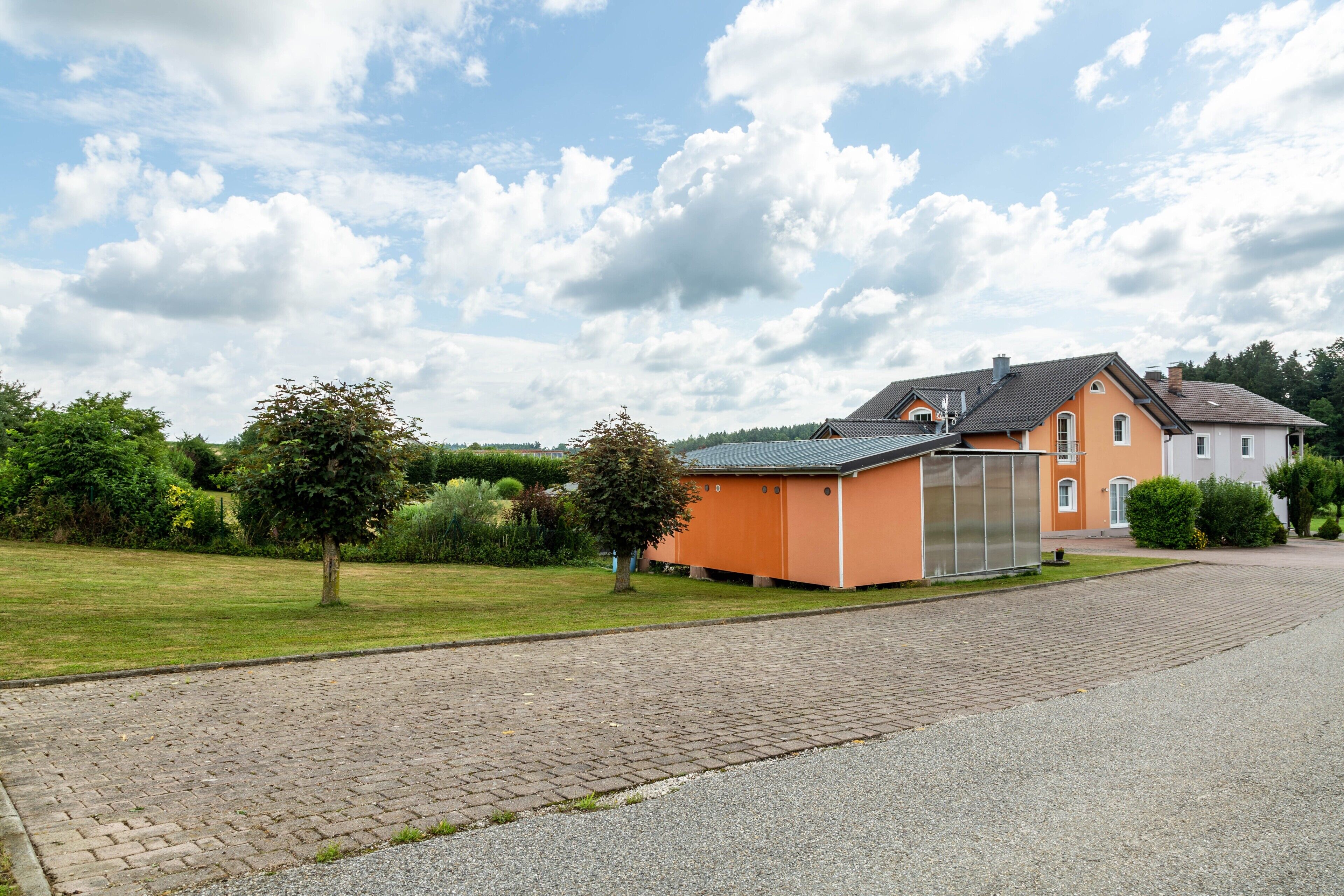 A residential area with a paved driveway, a house with a grey roof, and a small orange building.