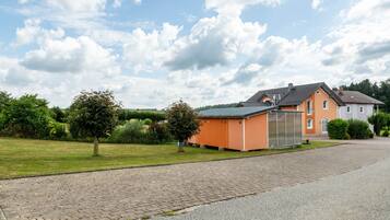 A residential area with a paved driveway, a house with a grey roof, and a small orange building.