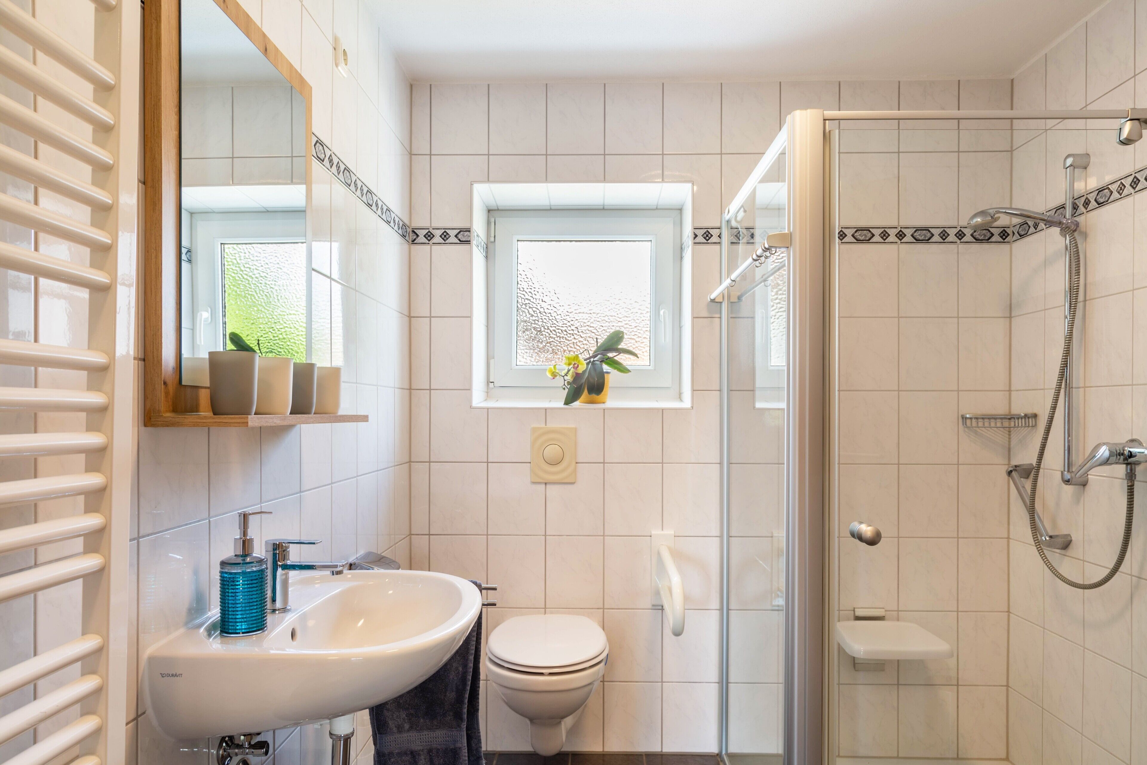 Een badkamer met een wastafel, toilet, douche en een raam met een plant.