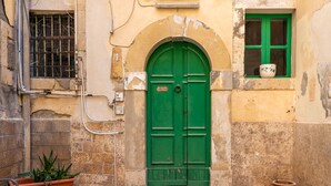 A green door with a small window above it, a potted plant to the left, and a potted plant to the right. - La Casa di Nonna Anna by Wonderful Italy (Syracuse)