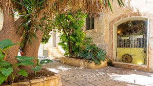 A courtyard with a large tree, potted plants, and a building with a window displaying masks. - La Casa di Nonna Anna by Wonderful Italy (Syracuse)