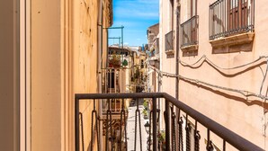 A narrow street with buildings on either side, featuring balconies with wrought iron railings and potted plants. - La Casa di Nonna Anna by Wonderful Italy (Syracuse)