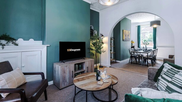 Una sala de estar con paredes verde azulado, una mesa de centro de madera, un televisor y un comedor con mesa y sillas.