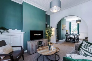 Ein Wohnzimmer mit türkisfarbenen Wänden, einem Holztisch, einem Fernseher und einem Essbereich mit Tisch und Stühlen.