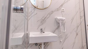 Ein Badezimmer mit einem weißen Waschbecken, einem an der Wand befestigten Föhn und einem Spiegel mit goldener Rahmung.