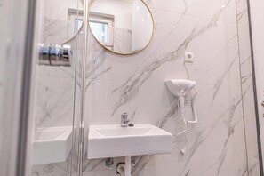 A bathroom with a white sink, a hairdryer mounted on the wall, and a mirror with a gold frame.