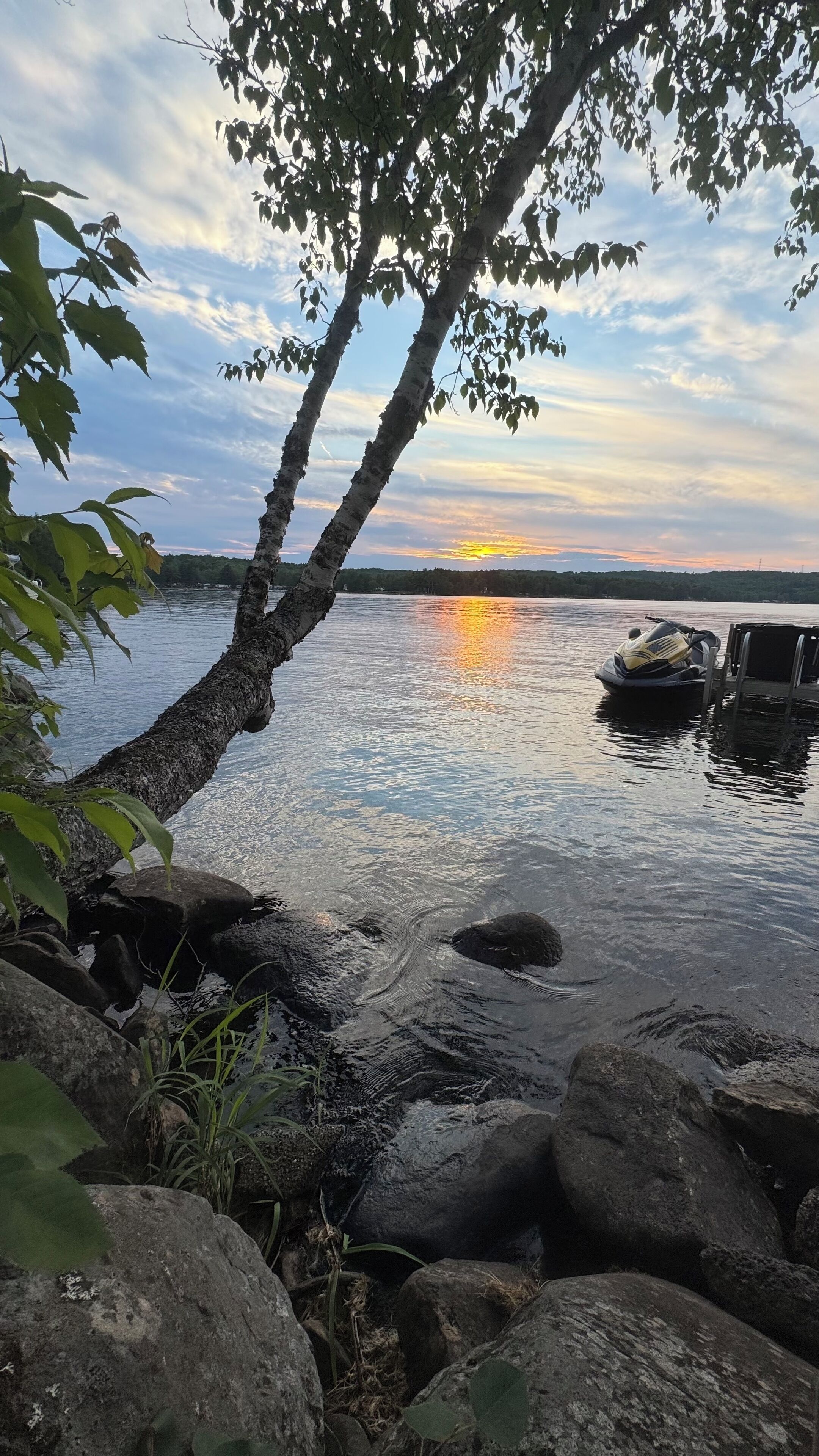 A serene lakeside scene with a sunset, calm water, and a boat docked on the right.