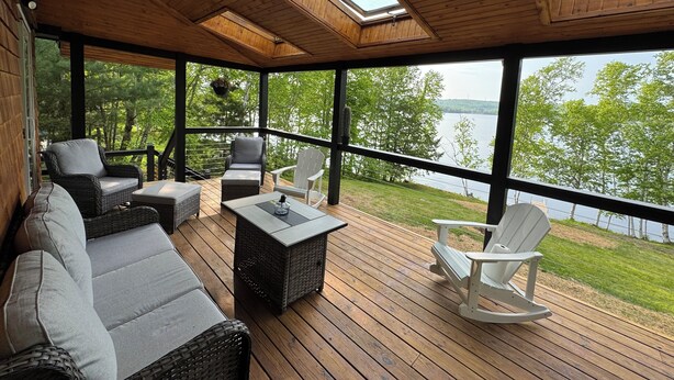 A covered deck with wicker furniture, a table, and a view of a lake.