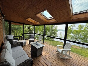 A covered deck with wicker furniture, a table, and a view of a lake.