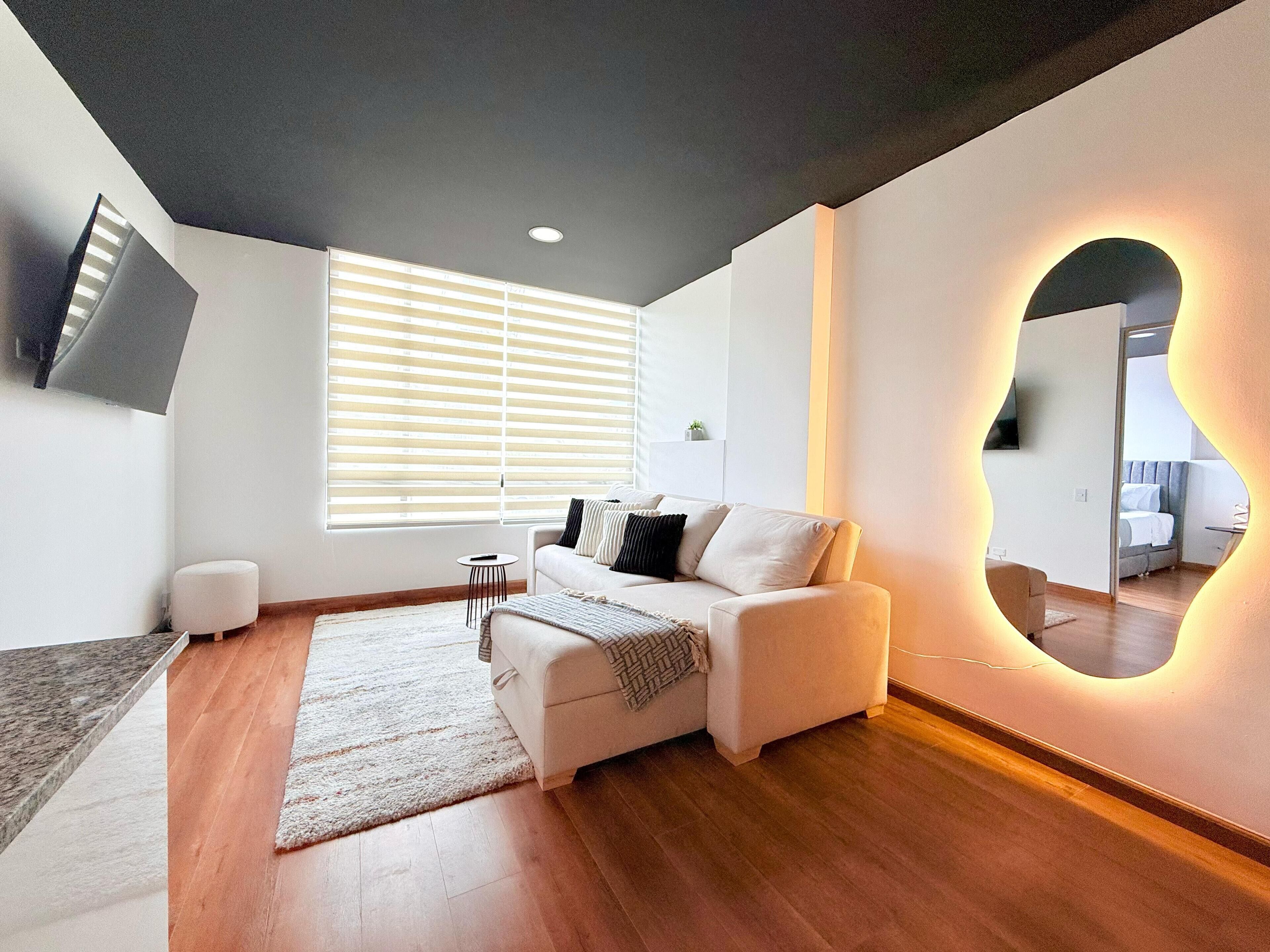 A modern living room with a sofa, a coffee table, a rug, and a large mirror with a unique light design.