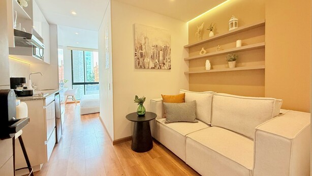 A modern living room with a white sofa, a small round table, and a cityscape painting on the wall. - KD Otoño by Weeki (Bogotá)