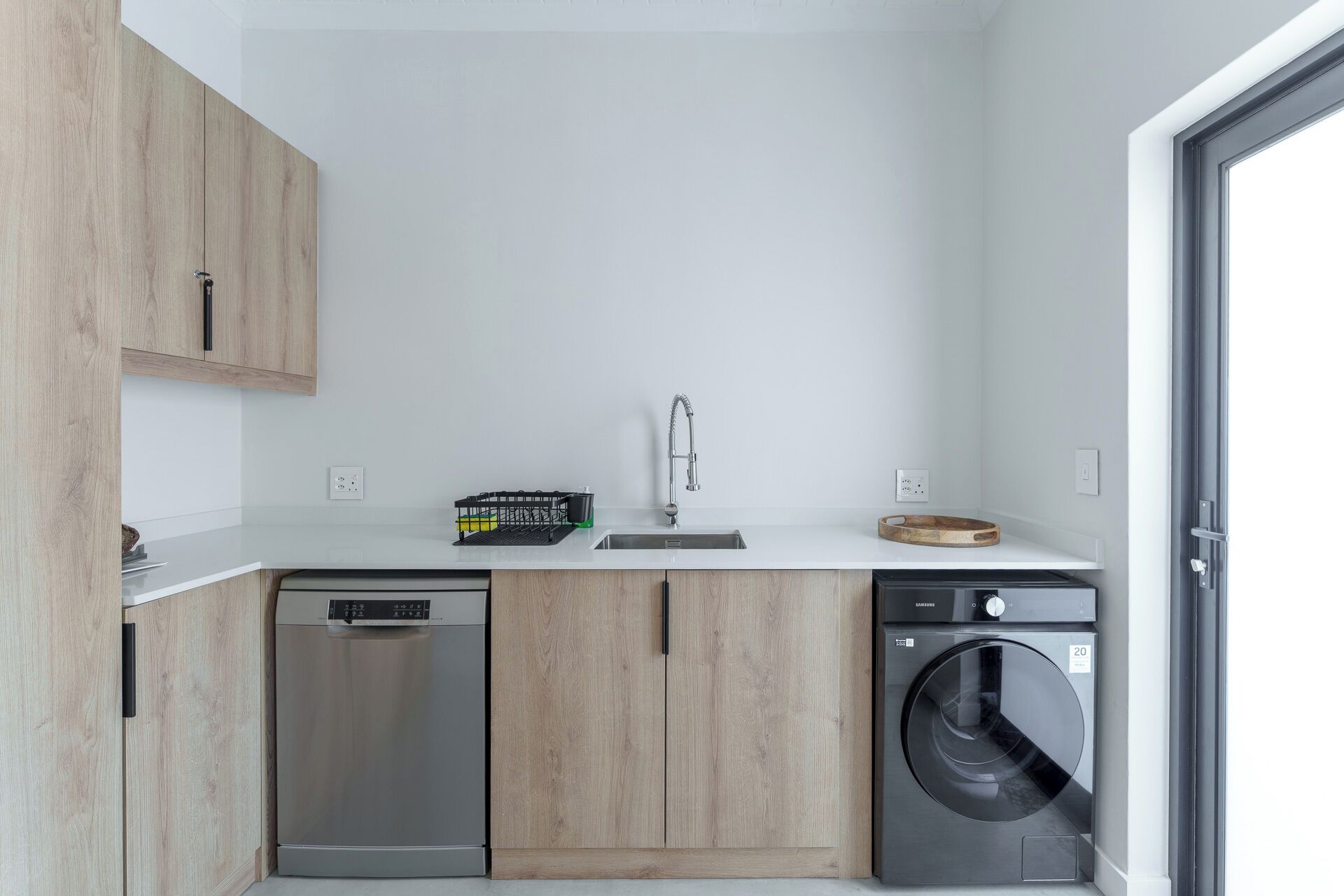 A compact kitchen with a dishwasher, washing machine, and a sink with a faucet.