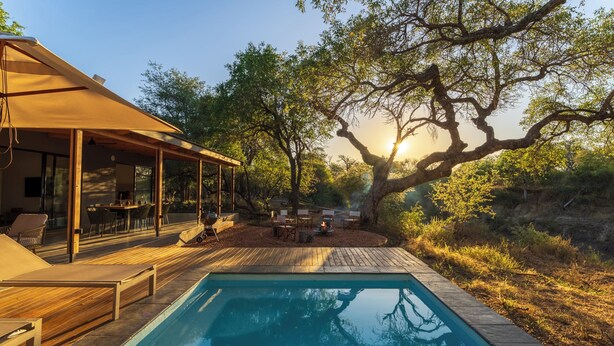 Ein Poolbereich mit überdachter Sitzgelegenheit, Holzterrasse und einem großen Baum.