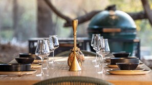 A dining table set with wine glasses, bowls, and a decorative centerpiece. - Nomads Den - Safari Villas in Hoedspruit (Hoedspruit)
