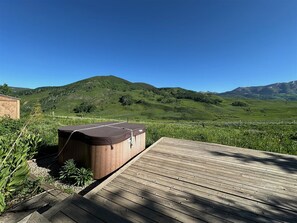 A wooden deck with a hot tub and a view of green hills.