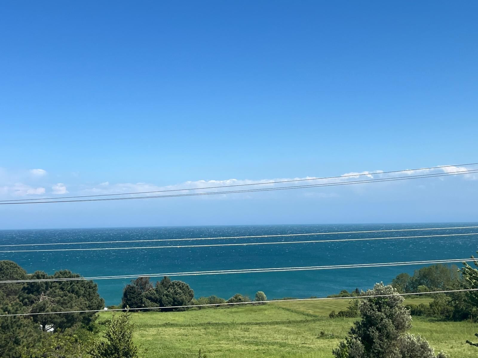 A coastal landscape with a clear view of the sea and power lines.