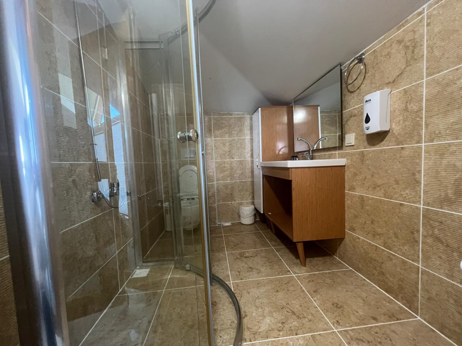 A bathroom with a glass-enclosed shower, a wooden vanity with a sink, and a toilet.