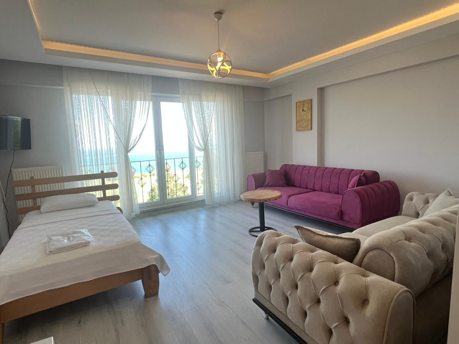 A hotel room with a bed, a sofa, a small table, and a balcony with a view.