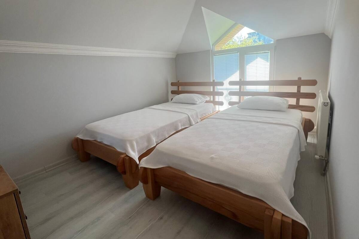 A bedroom with two wooden beds, a window with blinds, and a radiator.