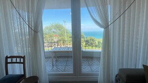 Um quarto com uma janela grande, uma cadeira de madeira, um banquinho pequeno e um sofá.