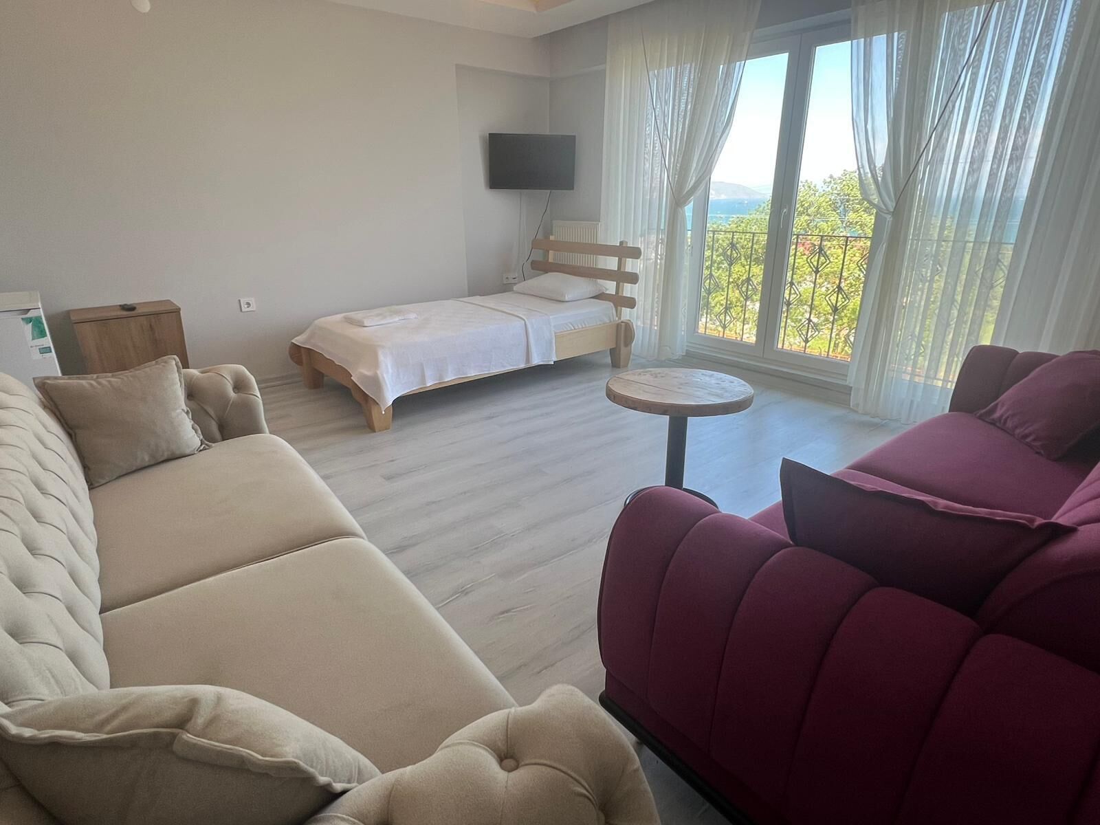 A modern bedroom with a bed, a sofa, a small round table, and a TV.