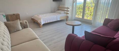 A modern bedroom with a bed, a sofa, a small round table, and a TV.