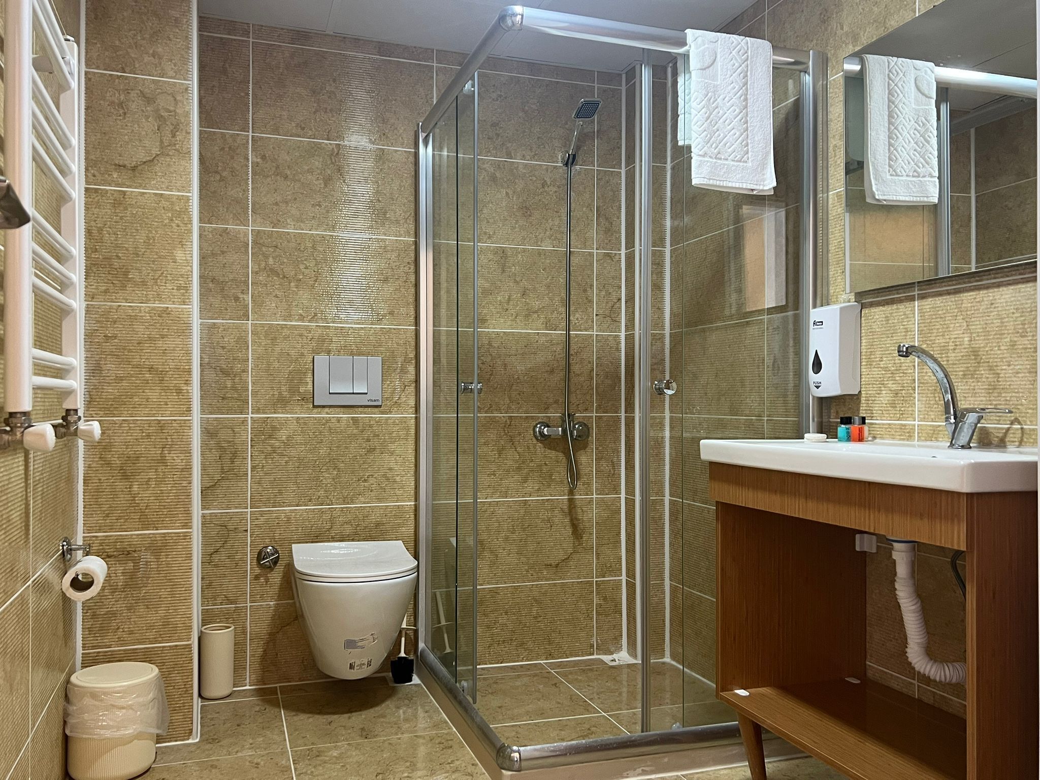 Un baño moderno con ducha de vidrio, inodoro, lavamanos con espejo y un perchero para toallas.