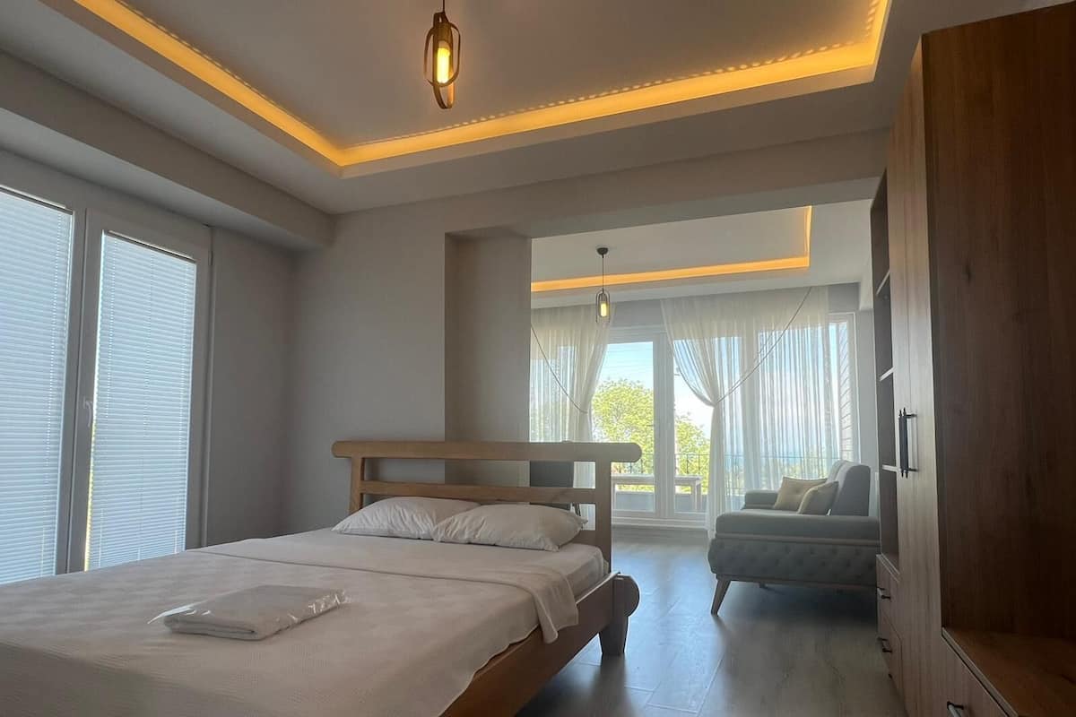 A bedroom with a bed, a wooden wardrobe, and a view of the outdoors.