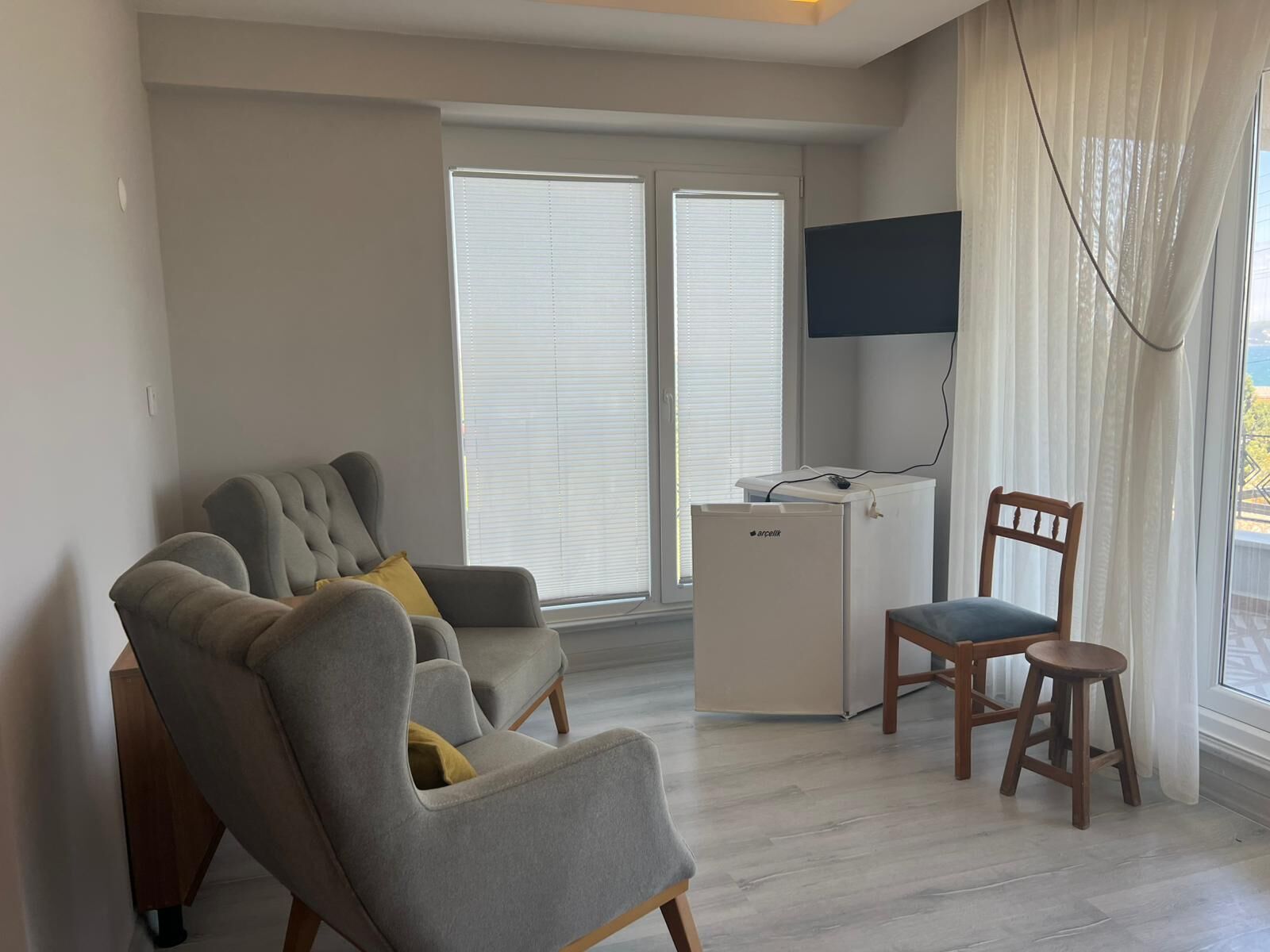 A living room with a grey sofa, a wooden chair, a small white table, and a TV mounted on the wall.