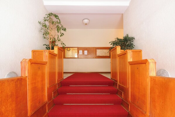 A staircase with wooden railings and red carpet leading to a room with a white ceiling and a plant on the wall.