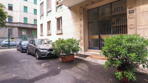 Un bâtiment doté d’une grande fenêtre et d’une porte, une voiture garée et deux plantes en pot.