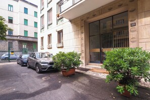 A building with a large window and a door, a parked car, and two potted plants.